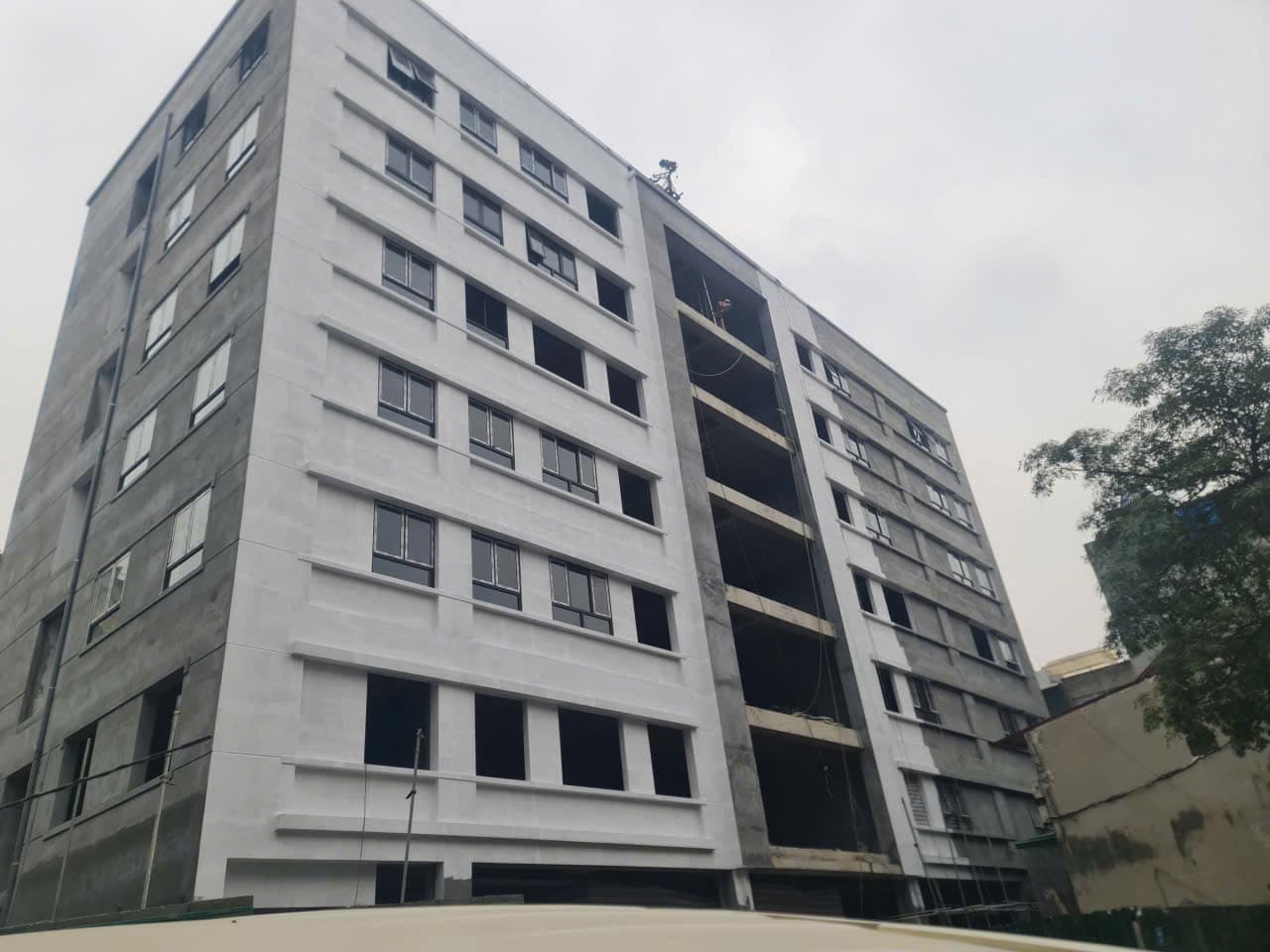 Chung cư bảy tầng mặt ngoài trát dở, cửa kính đã lắp, giàn giáo dựng phía trước.
