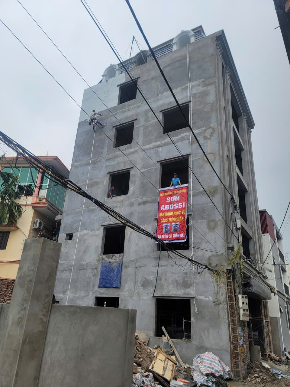 Công trình thô nhiều tầng treo băng rôn sơn, hai thợ làm việc trên tầng cao.