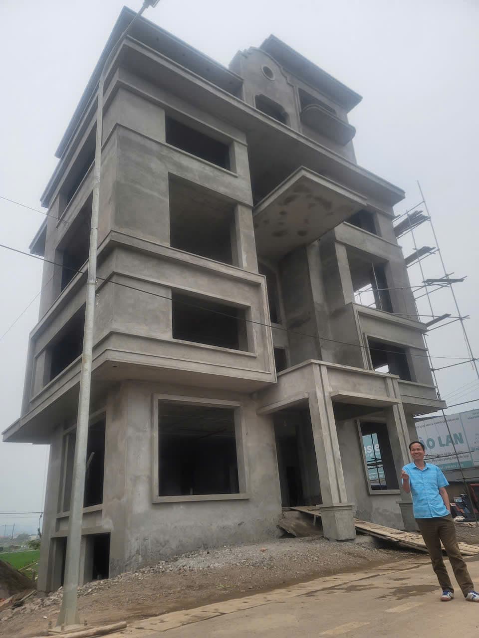 Công trình bốn tầng để trần kết cấu bê tông, một người đứng giơ tay trước mặt tiền.