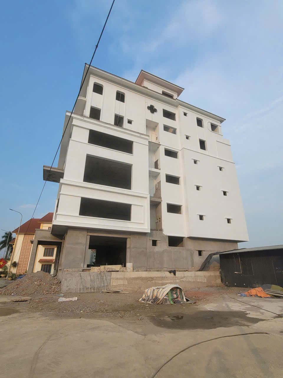 Nhà cao tầng bảy tầng đang hoàn thiện, tường đã trát trắng một phần, phần còn lại để trần.